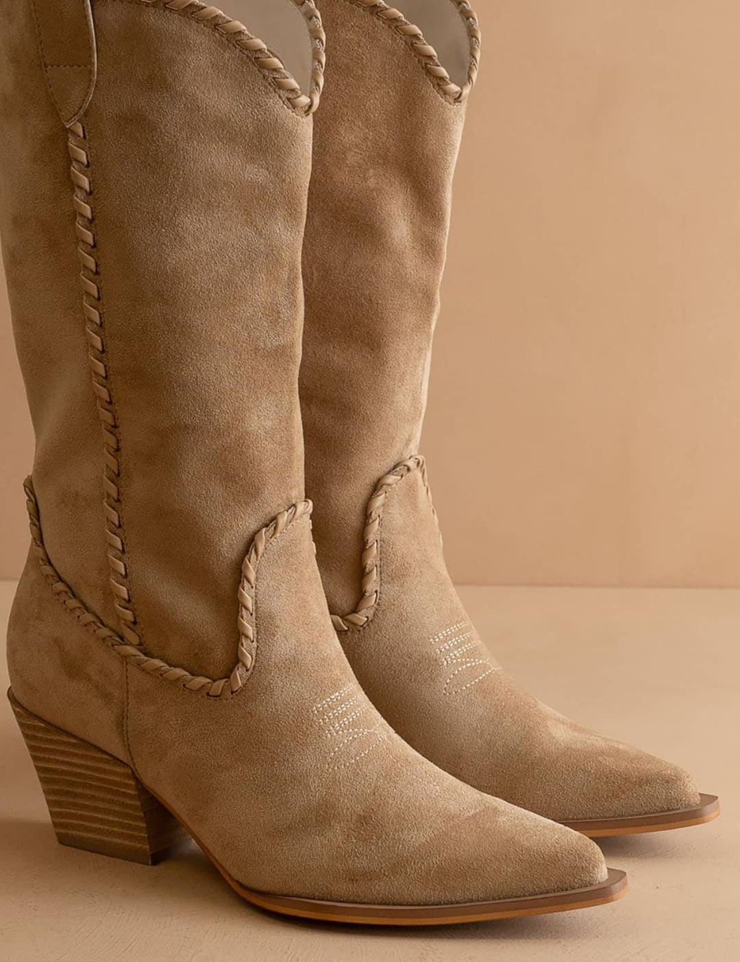 Beige suede cowboy boots with braided detailing and a stacked heel.