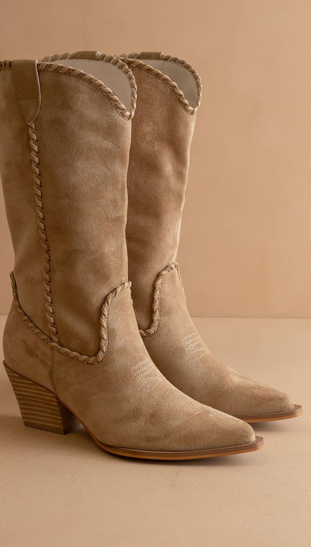 Beige suede cowboy boots with braided detailing and a stacked heel.
