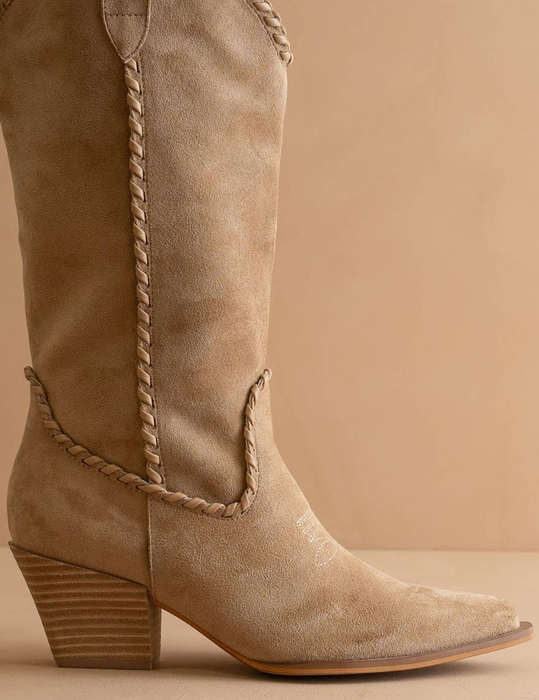Beige suede cowboy boot with braided leather detailing and a stacked heel.