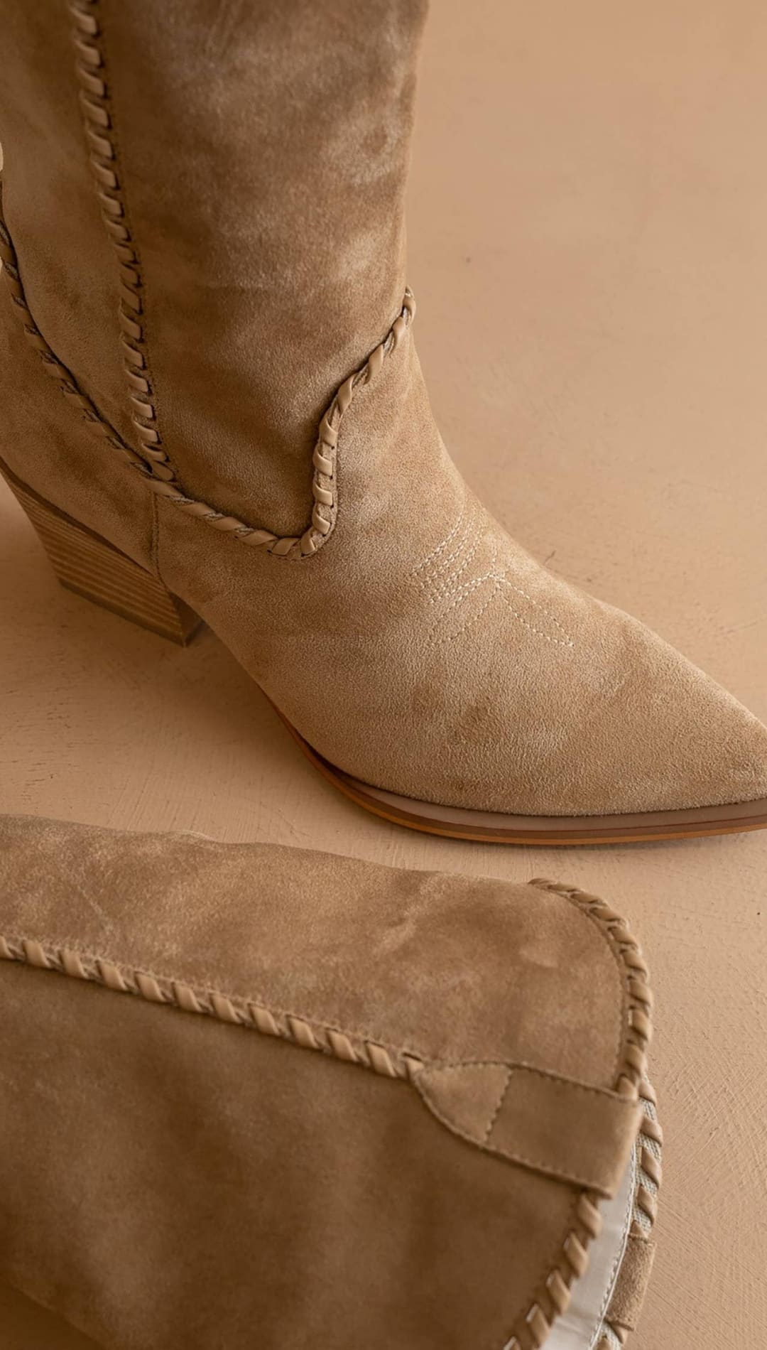 Tan suede cowboy boot with a pointed toe and braided stitching along the shaft.