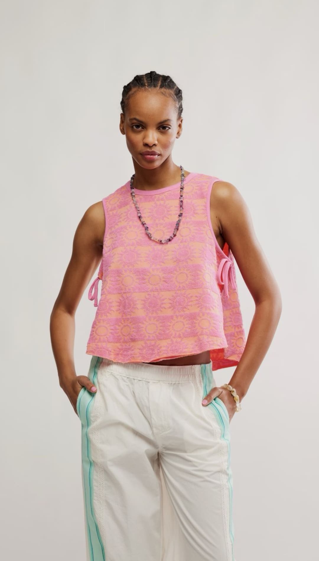Woman wearing a pink patterned sleeveless top and white pants.