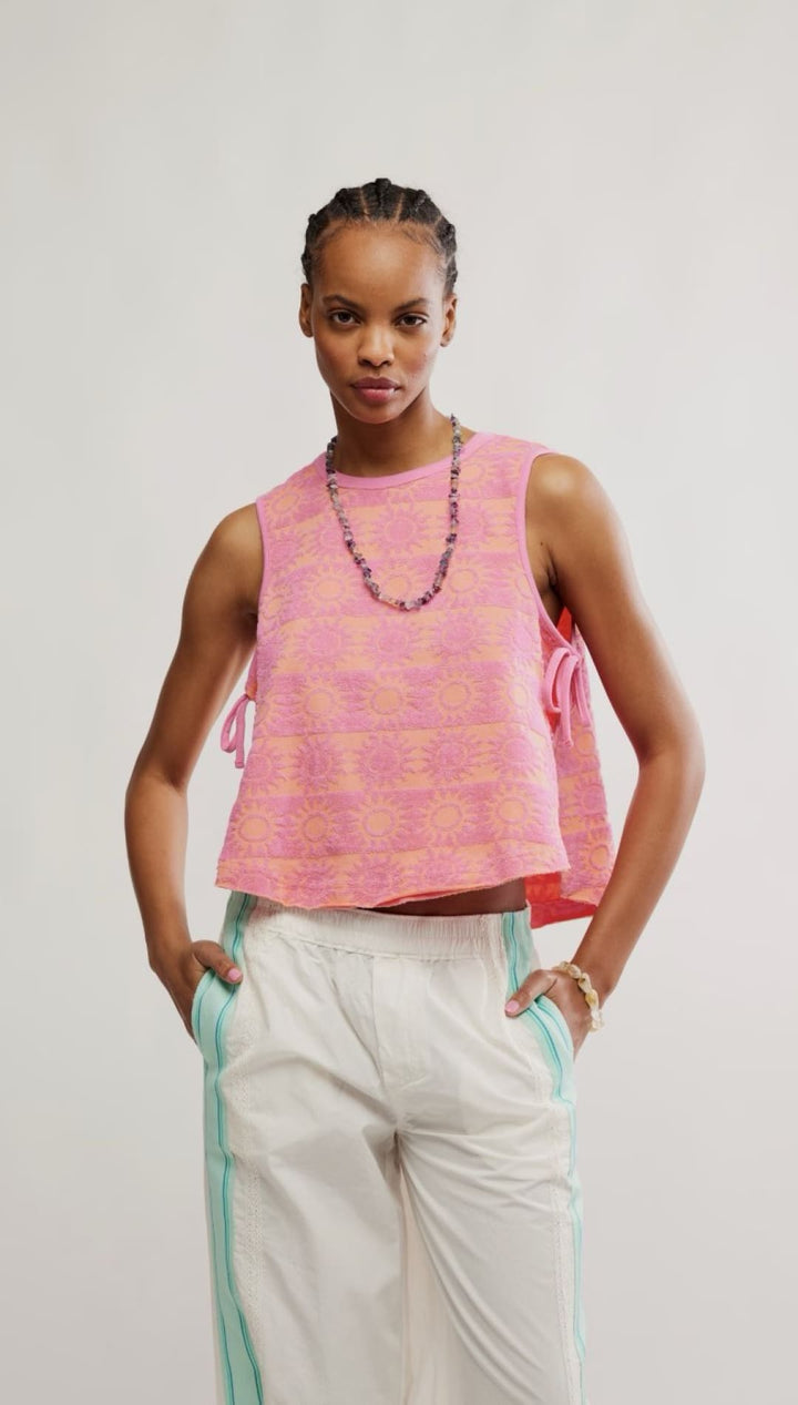 Woman wearing a pink patterned sleeveless top and white pants.