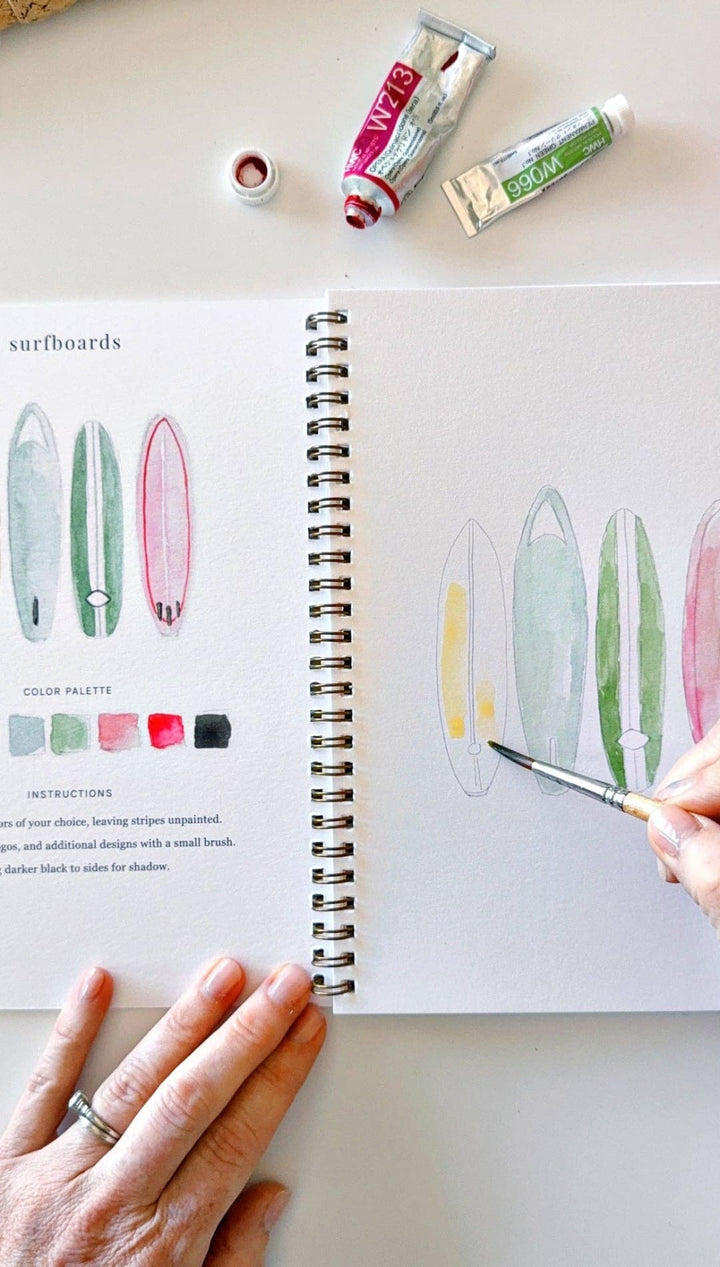 Watercolor paint set with tubes and brushes, pastel colors, wooden handles, spiral-bound sketchbook.