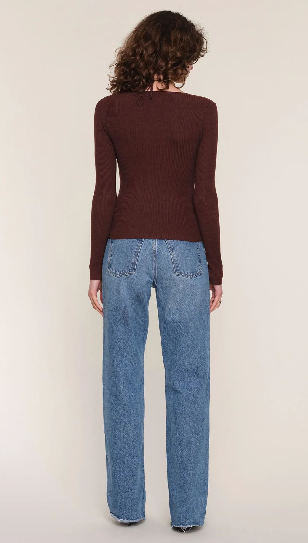 Brown long-sleeved sweater with a ribbed neckline and cuffs, light blue jeans with subtle floral embroidery.