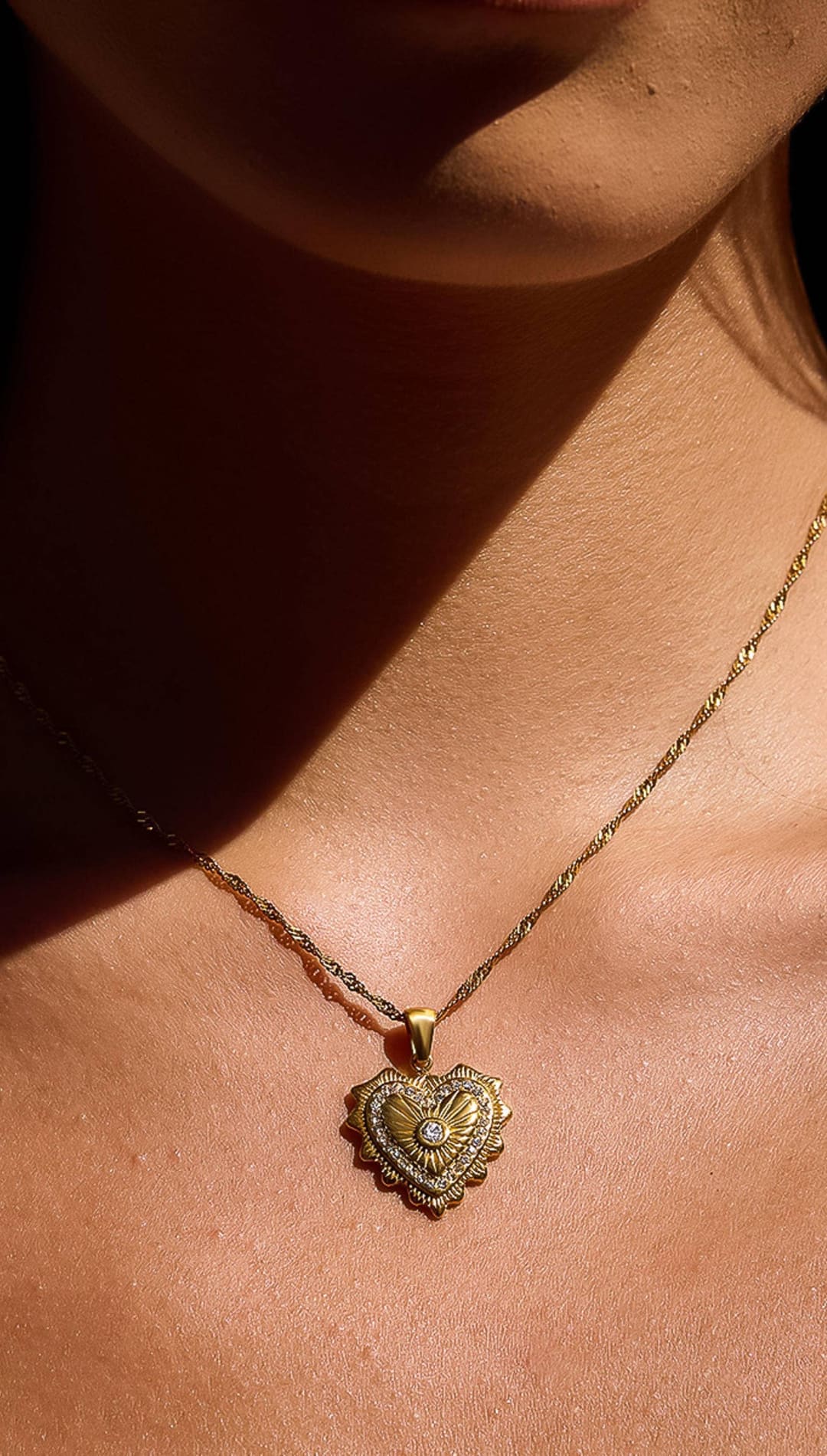 A delicate gold heart-shaped pendant necklace with intricate detailing and a central diamond.