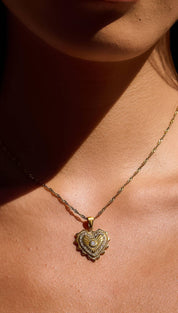 A delicate gold heart-shaped pendant necklace with intricate detailing and a central diamond.