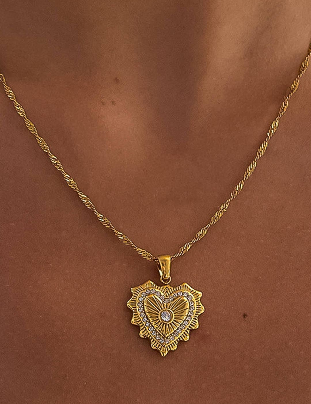 Gold heart-shaped pendant necklace with intricate sunburst detailing and a central diamond accent.