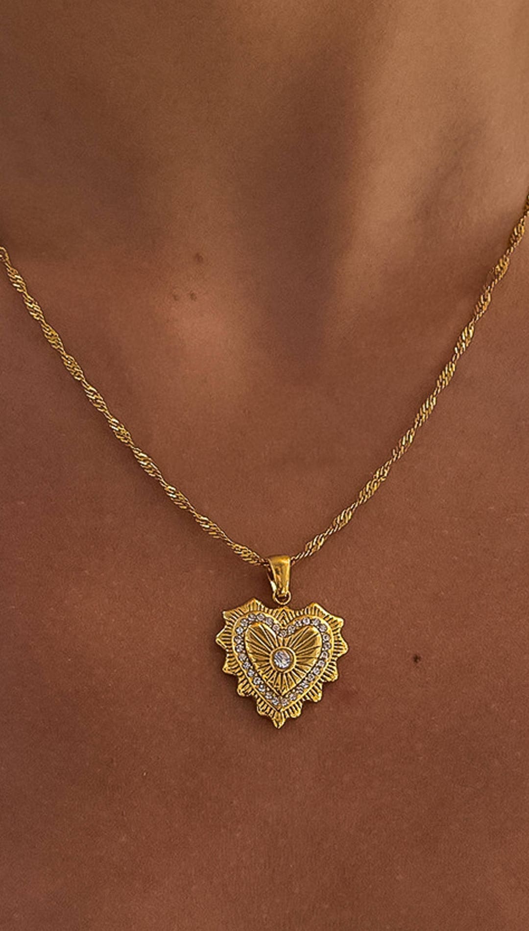 Gold heart-shaped pendant necklace with intricate sunburst detailing and a central diamond accent.