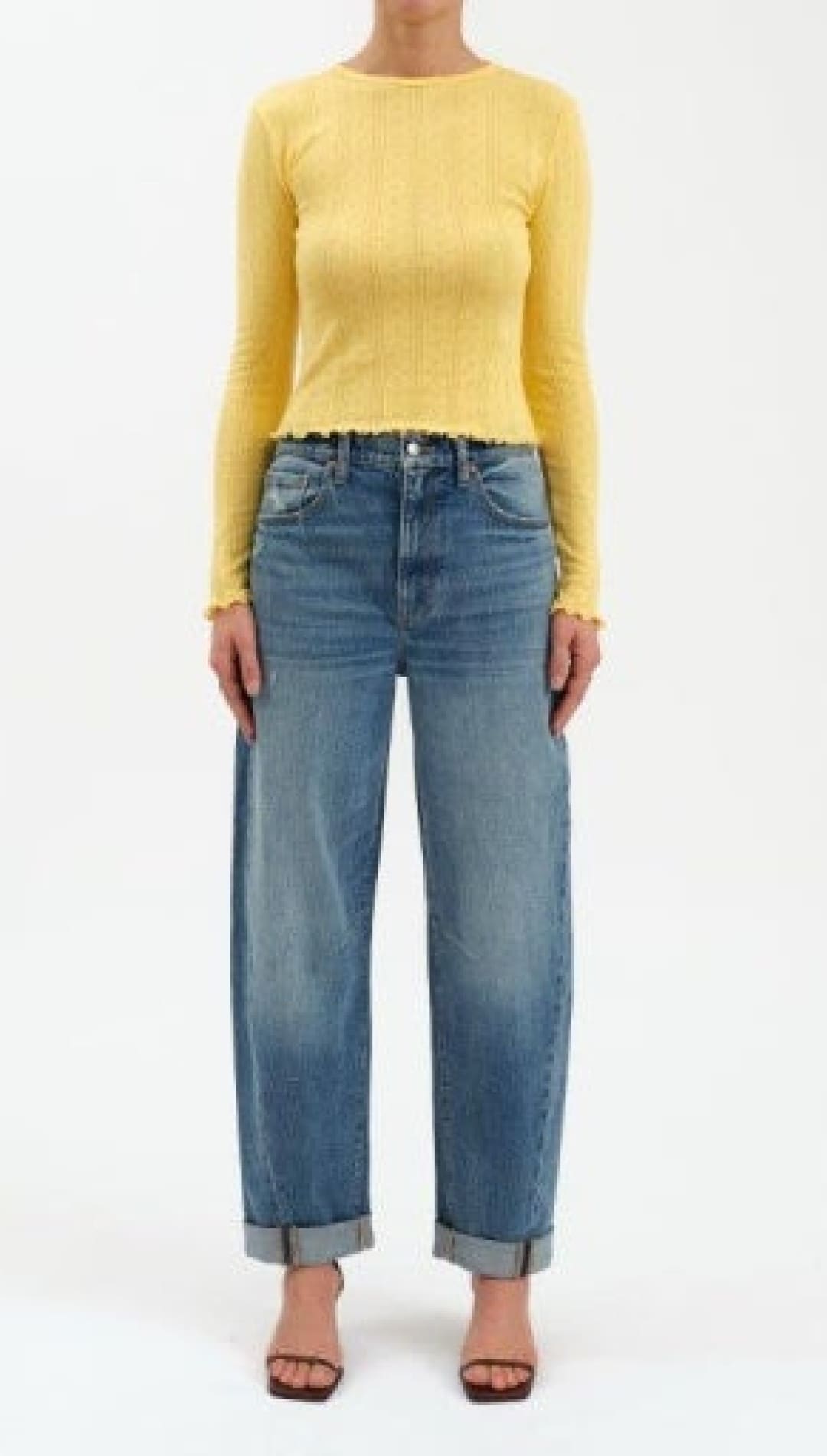 A woman models a long-sleeve yellow ribbed top with ruffled edges and cuffed blue jeans with brown high-heeled sandals.