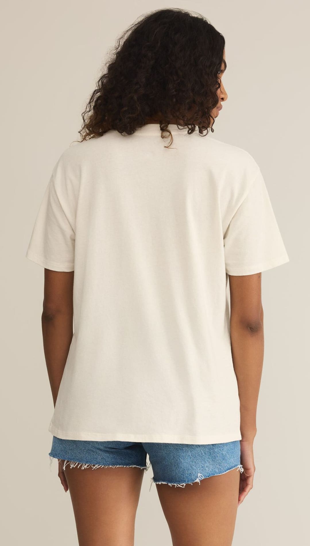 Woman wearing a cream-colored t-shirt and denim shorts.