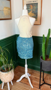 Blue sequined mini skirt worn with a cream halter top on a mannequin.