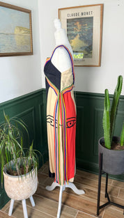 A vibrant, sleeveless maxi dress with bold geometric panels in black, beige, and red, accented by vertical rainbow stripes and a striking eye motif on the front.