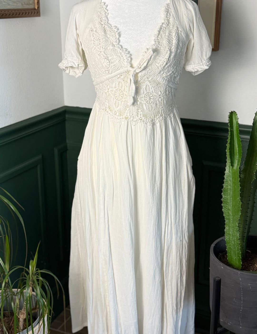 A flowing off-white midi dress with delicate lace detailing at the neckline and bodice, featuring short puffed sleeves and a gathered waist.