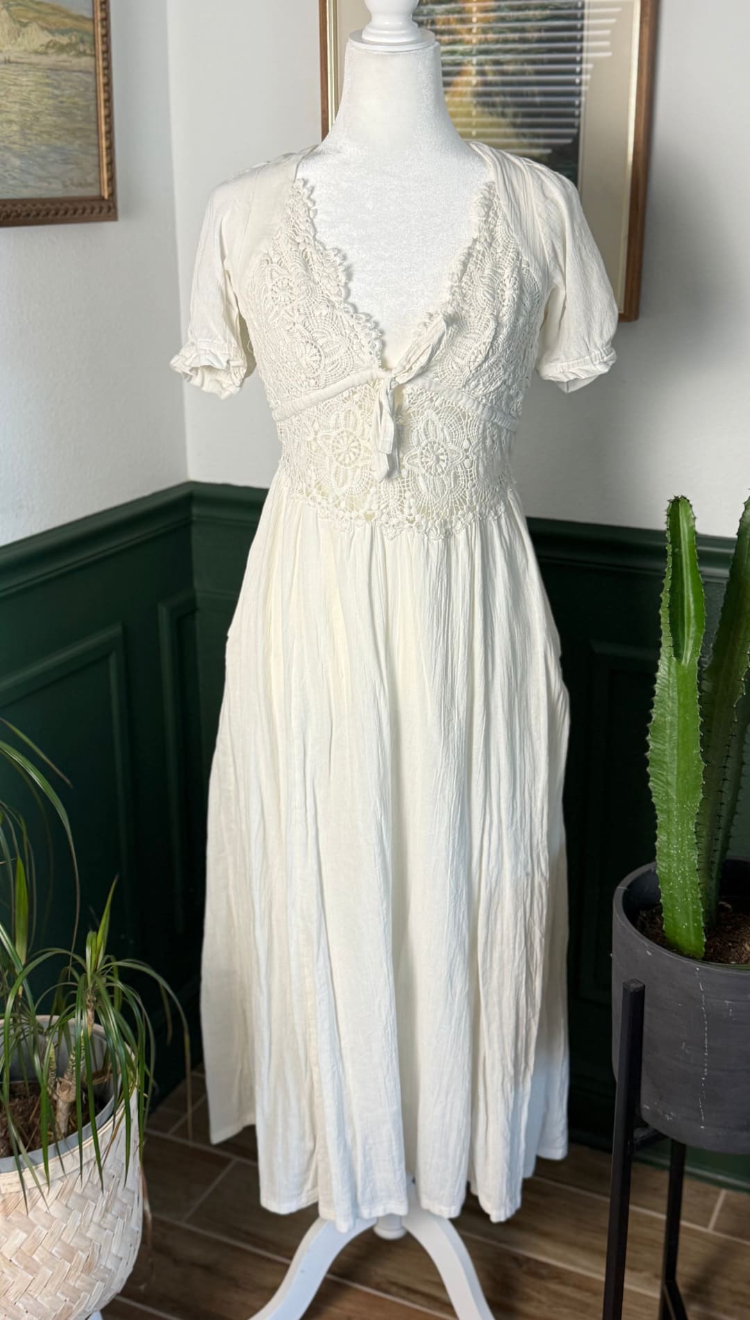 A flowing off-white midi dress with delicate lace detailing at the neckline and bodice, featuring short puffed sleeves and a gathered waist.