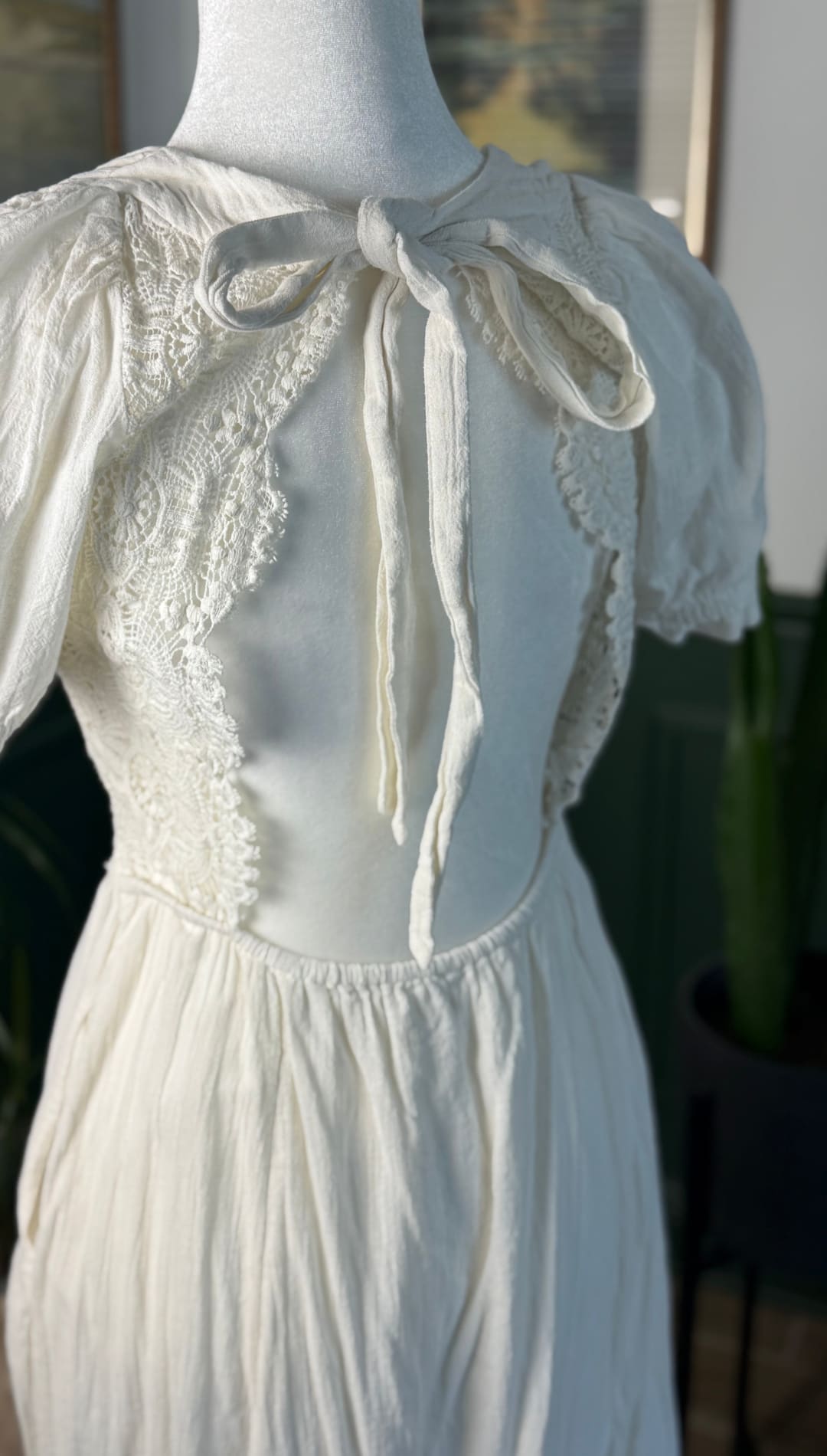 A delicate off-white lace-trimmed dress with a soft, flowing fabric and a charming bow at the neckline.