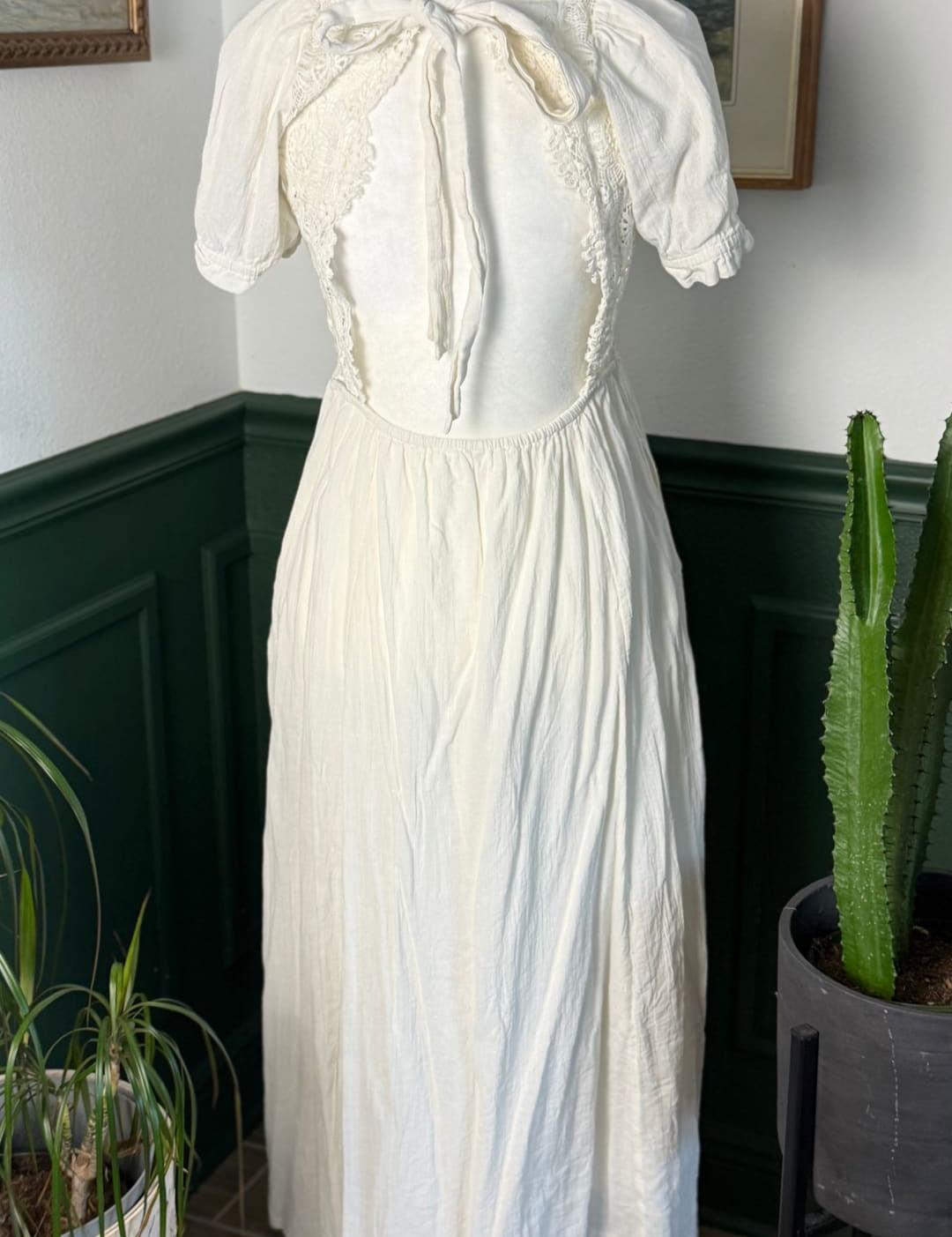 A vintage-style off-white dress with delicate lace detailing and a gathered waist, displayed on a mannequin.