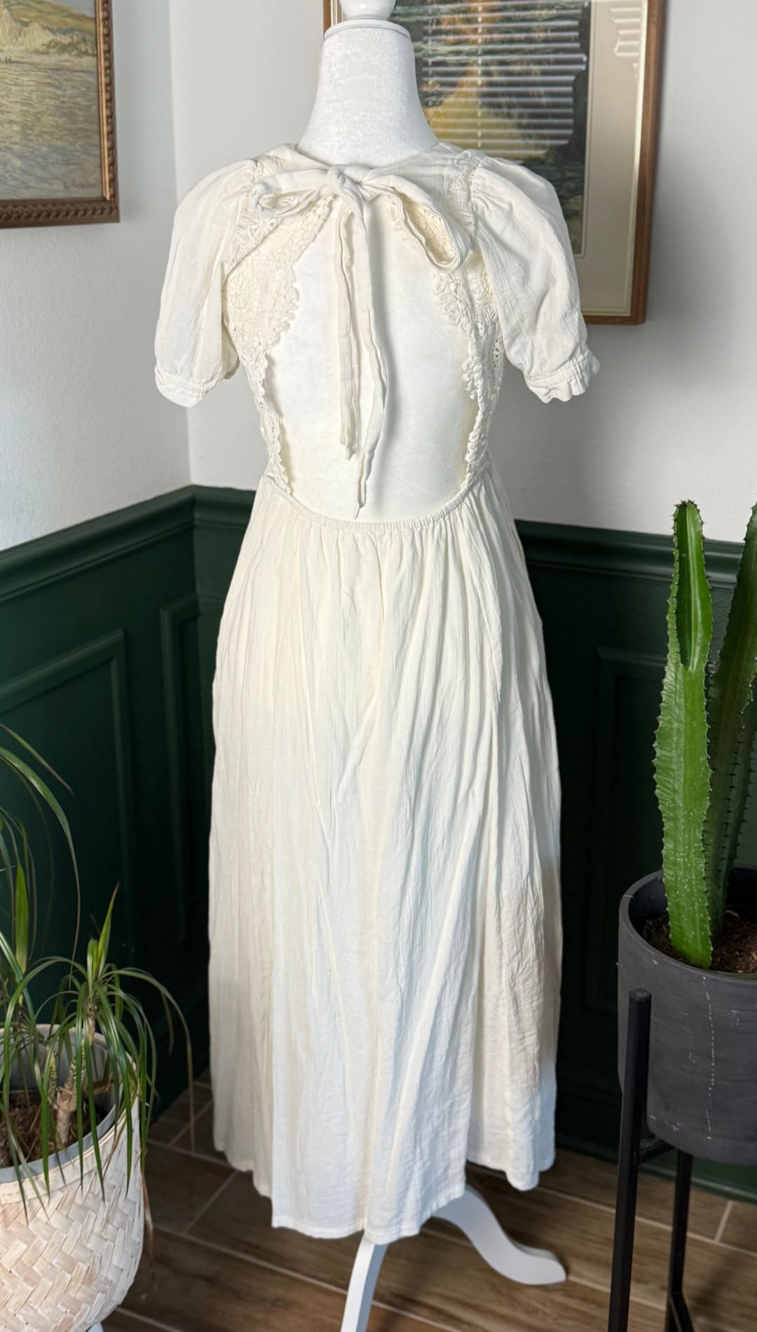 A vintage-style off-white dress with delicate lace detailing and a gathered waist, displayed on a mannequin.