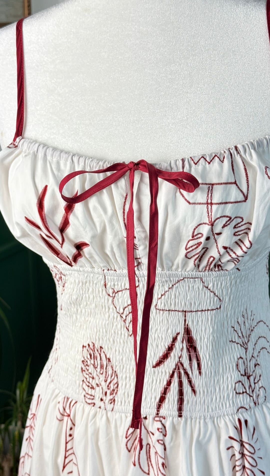 White sundress with red embroidered tropical foliage and a matching red ribbon tie at the back.