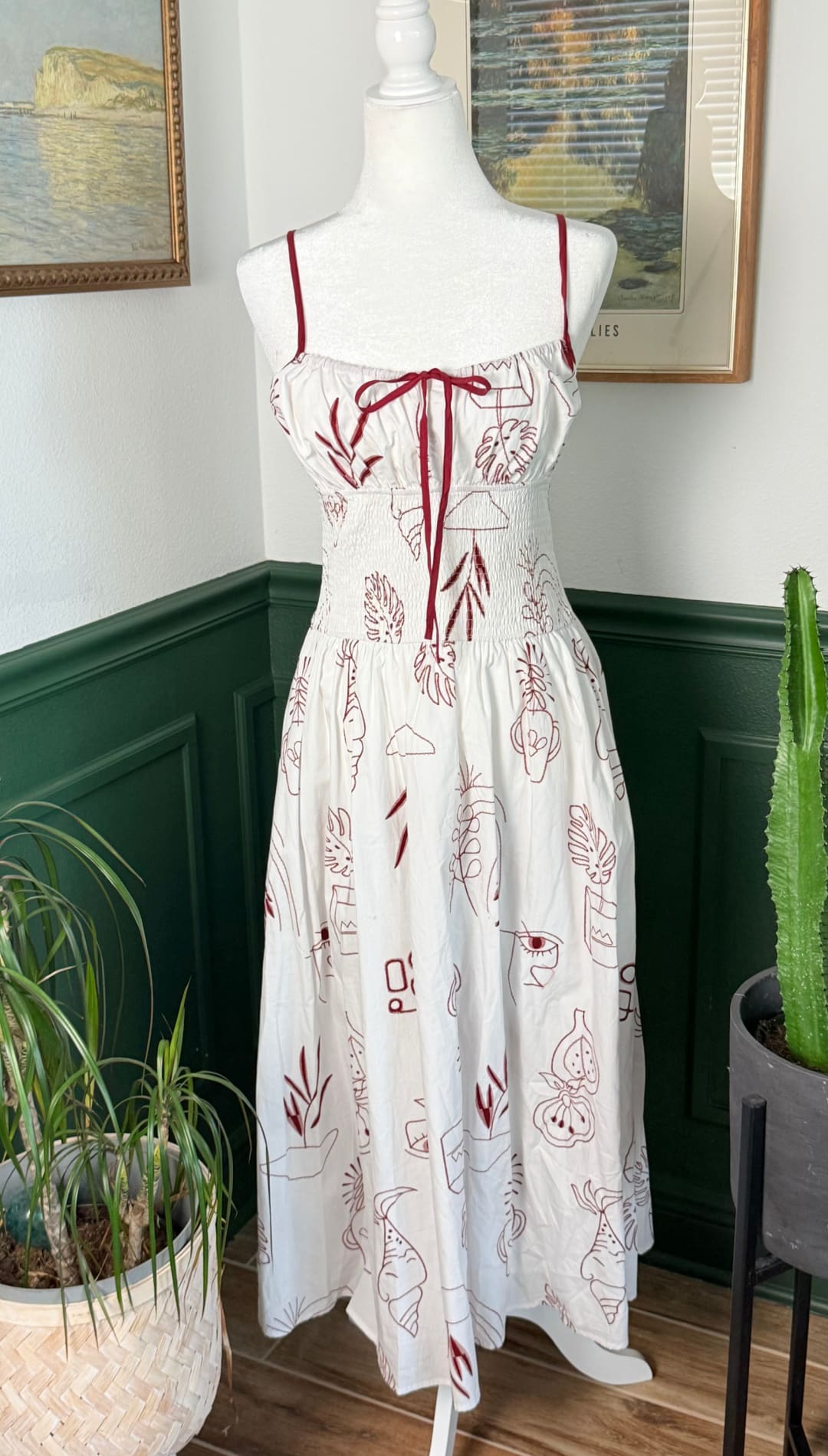 A white sundress with red embroidered botanical patterns and thin spaghetti straps, featuring a tied bow at the neckline.