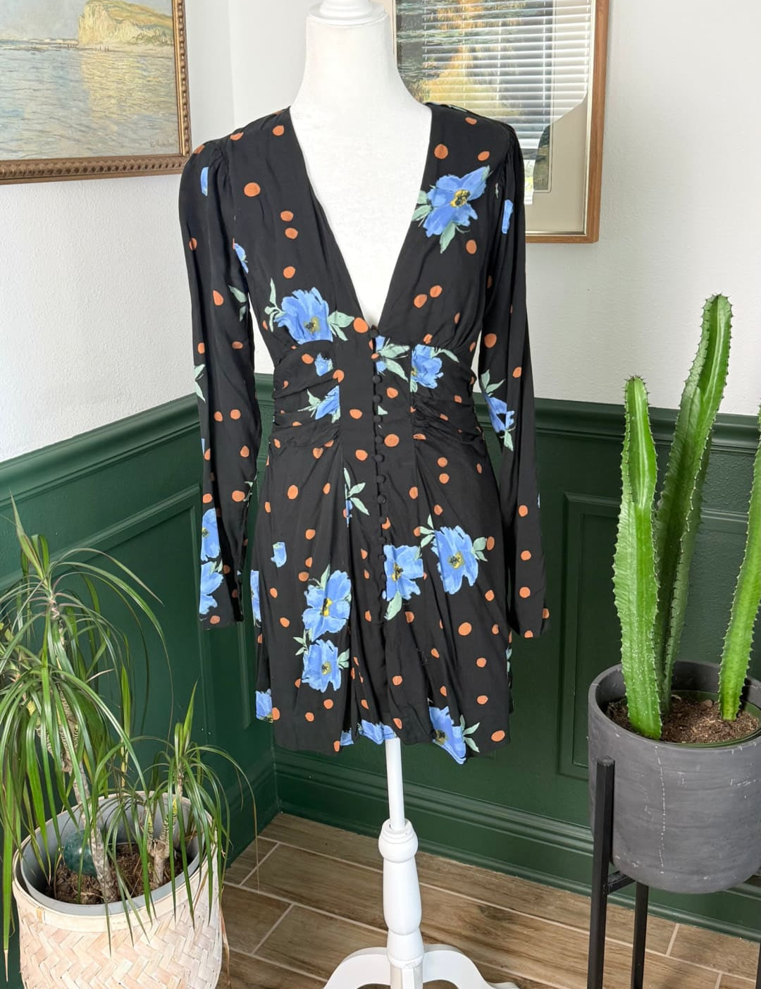 Black floral print dress with blue flowers and orange polka dots, long sleeves, v-neckline, and a ruched waist.