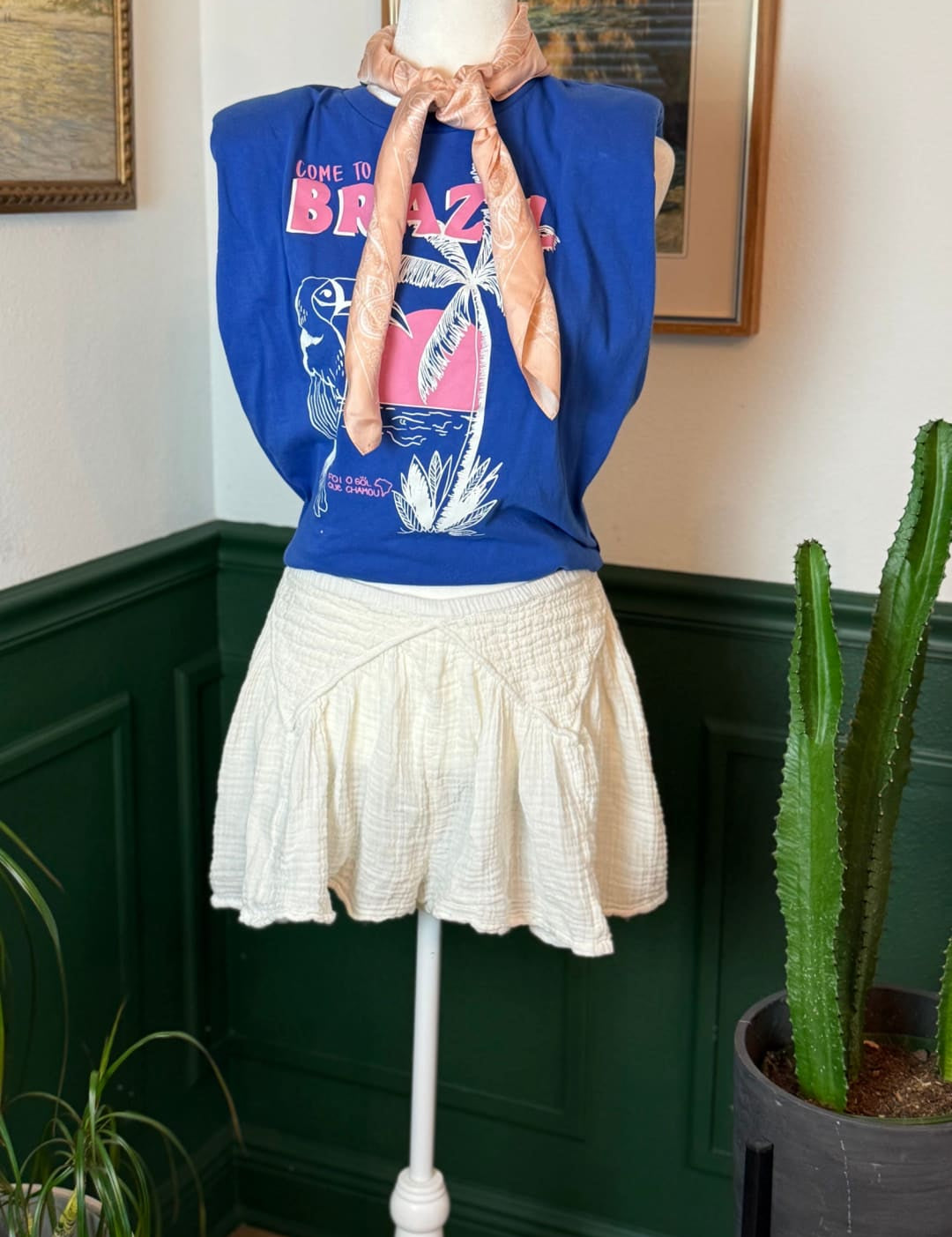 Blue sleeveless graphic tee with ’lone to brazil’ print and palm tree design, worn over a white ruffled skirt.