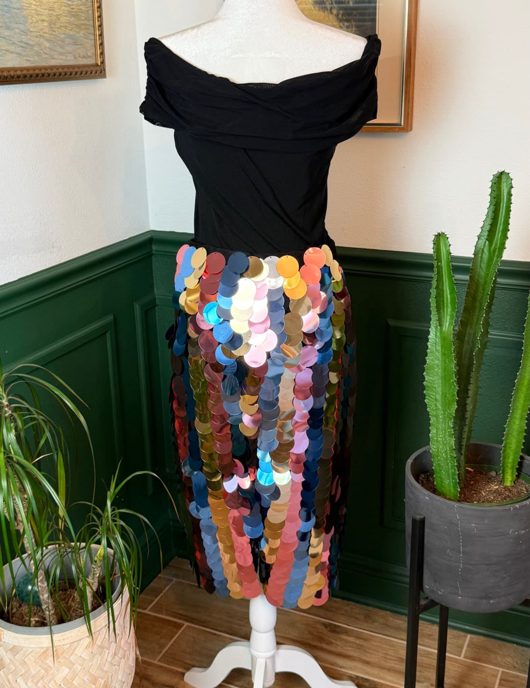 A vibrant, multicolored sequined midi skirt with a flowing, off-the-shoulder black top displayed on a white mannequin.