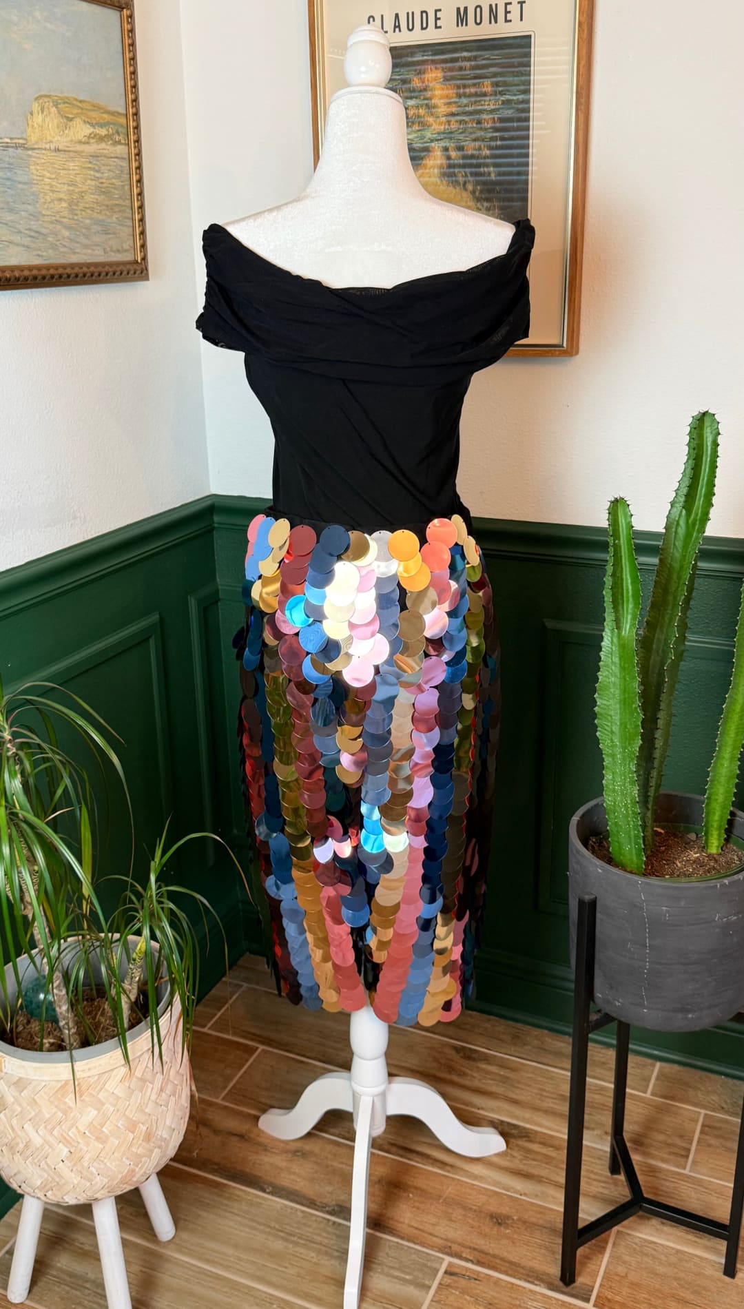 A vibrant, multicolored sequined midi skirt with a flowing, off-the-shoulder black top displayed on a white mannequin.
