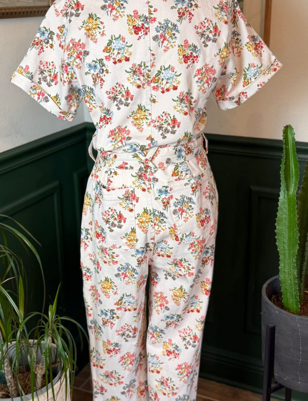 A vintage-style floral print jumpsuit in soft cream fabric, featuring short sleeves and a belted waist with rolled cuffs.