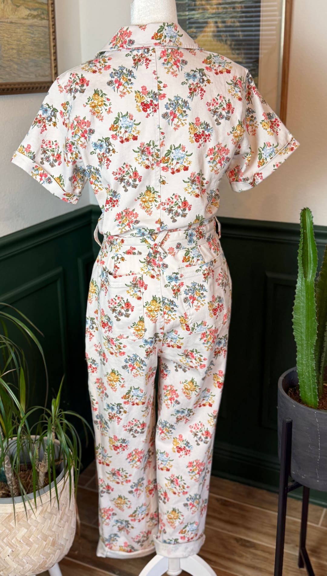 A vintage-style floral print jumpsuit in soft cream fabric, featuring short sleeves and a belted waist with rolled cuffs.
