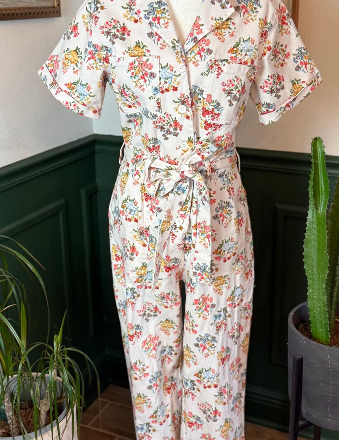 A soft, cream-colored floral print jumpsuit with short sleeves and a belted waist.