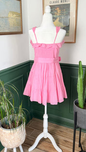 A vibrant pink, ruffled strap dress with a cinched waist and tiered skirt displayed on a white mannequin.