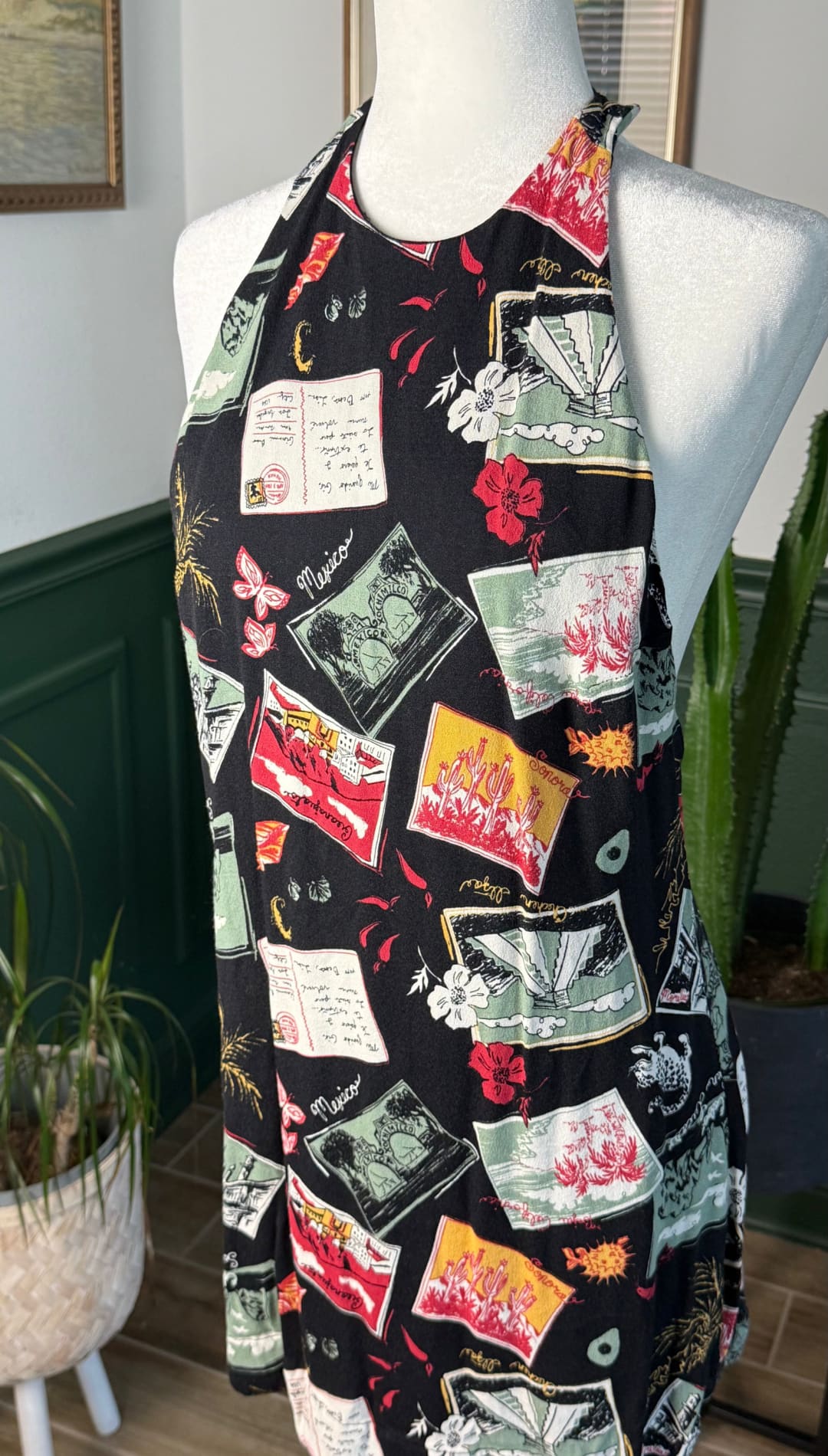 Black halter-neck dress adorned with a vibrant collage of vintage postcards and floral motifs in red, green, yellow, and white.