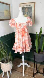 A coral and white printed off-the-shoulder mini dress with puffed sleeves and a tiered hemline.