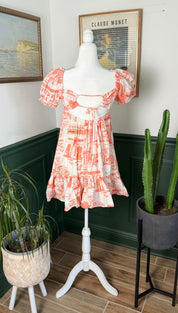 A coral and white printed dress with puffed sleeves, a square neckline, and ruffled hemline displayed on a mannequin.