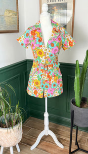 Vibrant floral print short-sleeved jumpsuit with a collar, belt, and pockets.