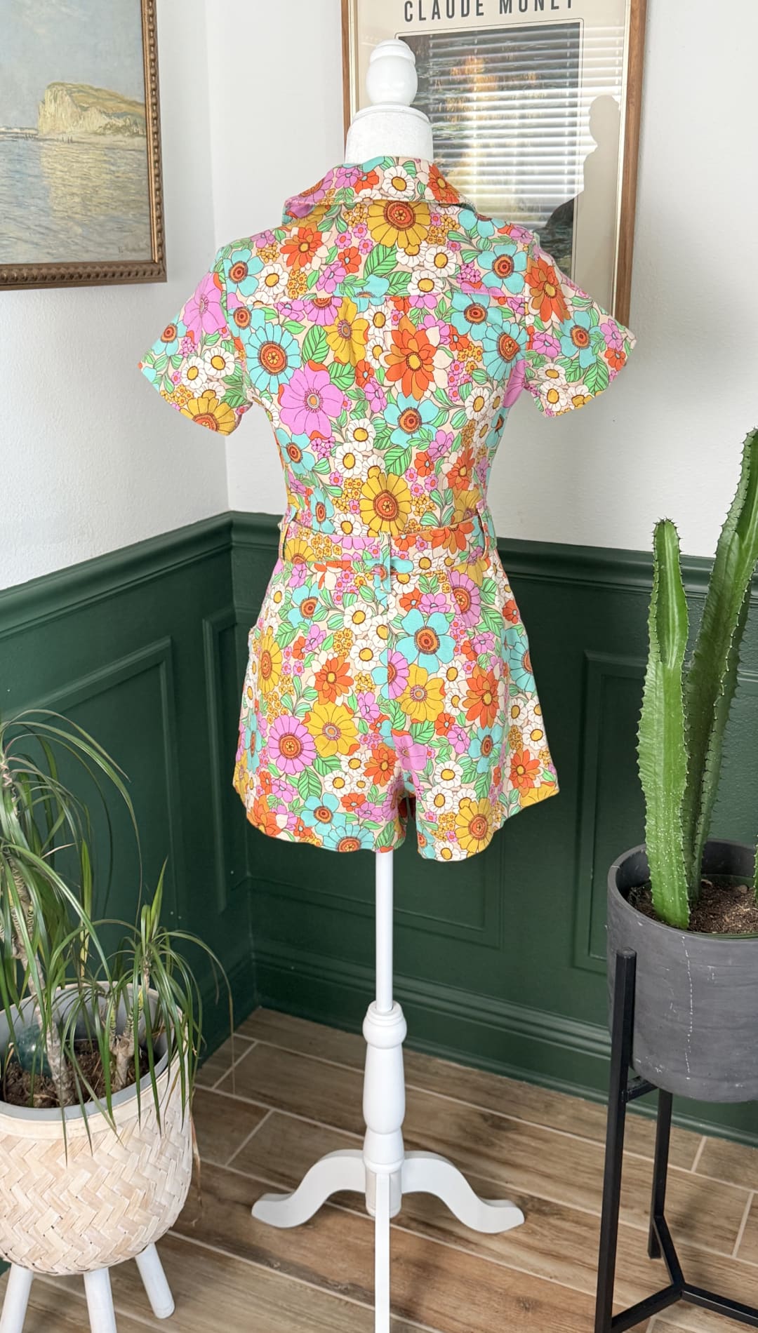 A vibrant floral print romper in shades of pink, orange, yellow, and turquoise with short sleeves and a collar.