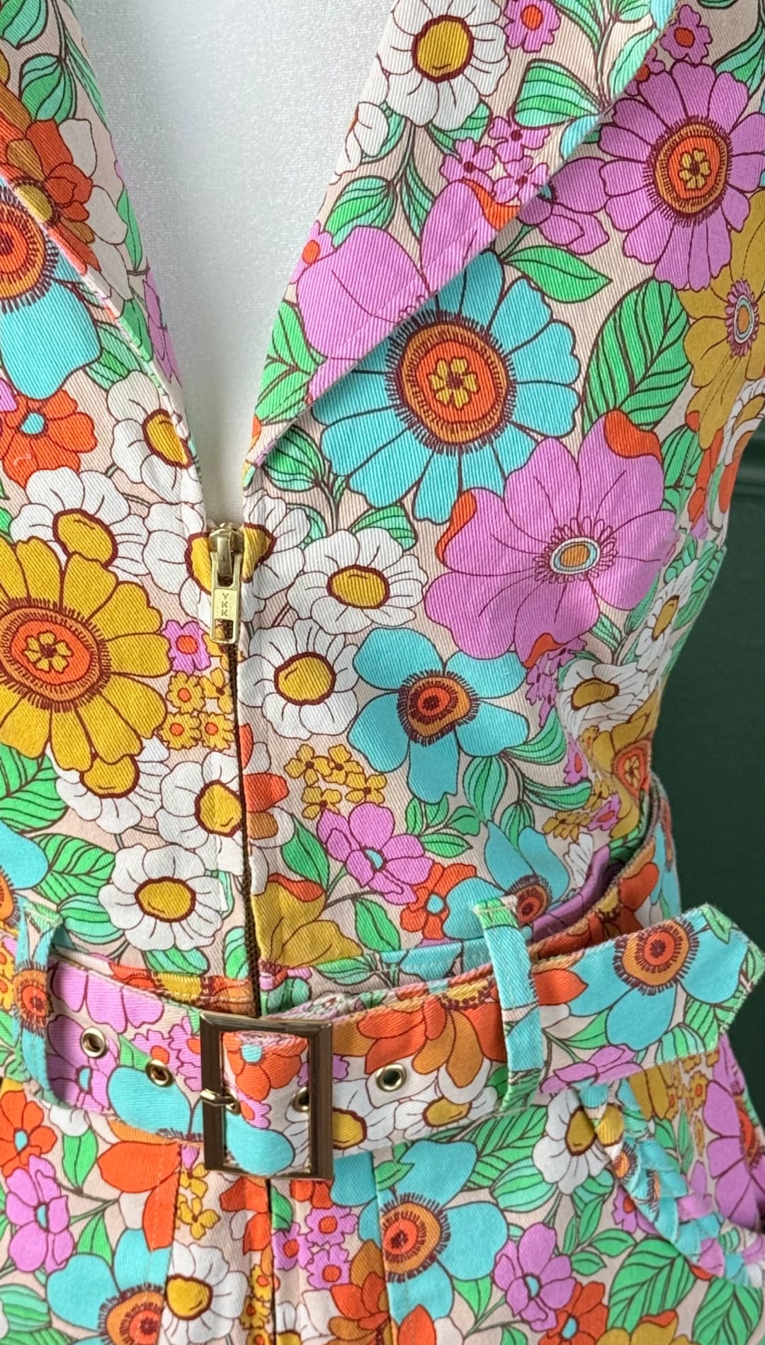 A vibrant, retro-style floral dress with a bold pattern of pink, blue, yellow, and orange flowers on a light beige background.