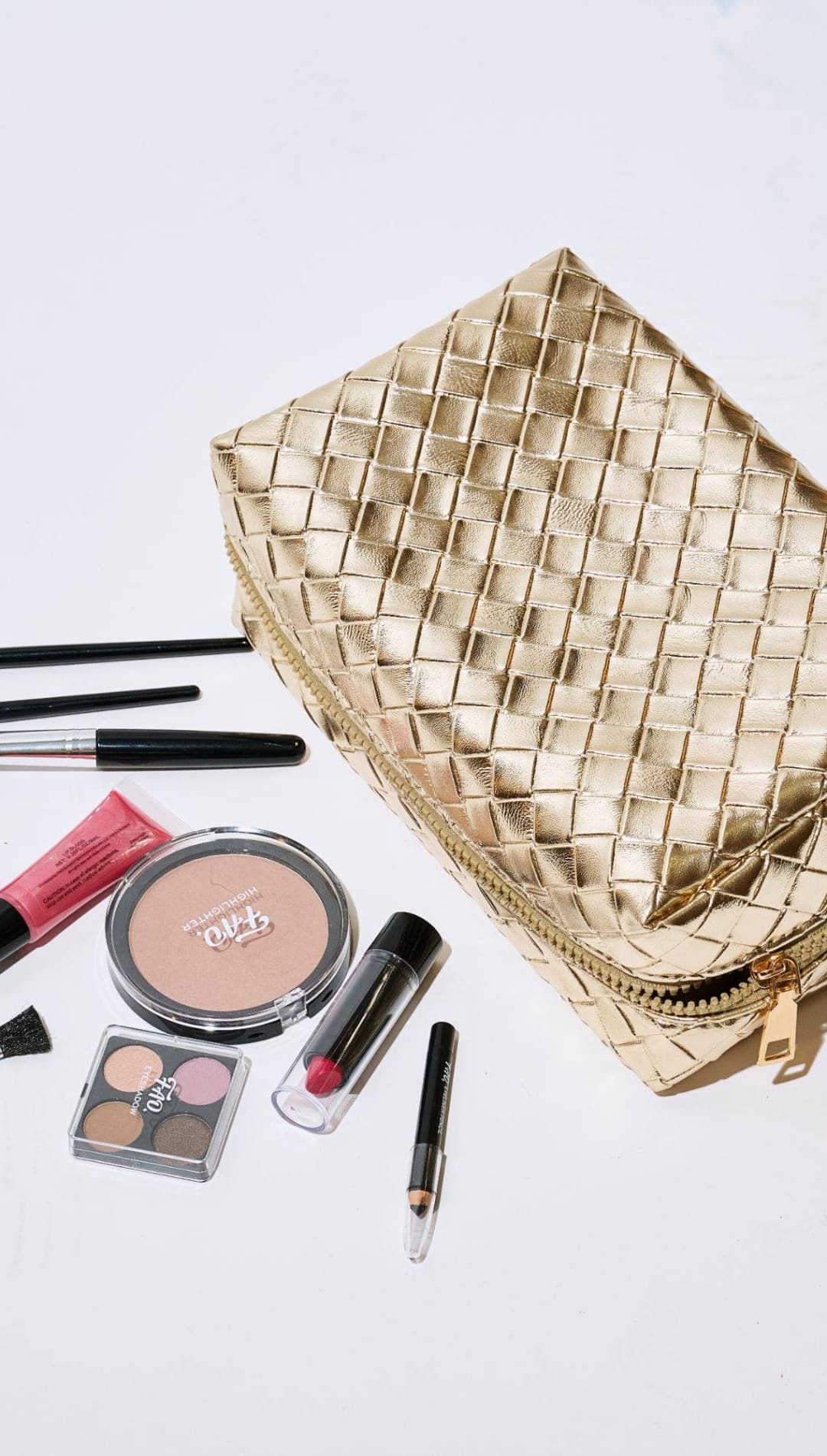 Gold quilted makeup bag with zipper closure and various cosmetics.