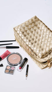Gold quilted makeup bag with zipper closure and various cosmetics.