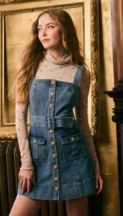 A light blue denim mini dress with a belted waist and front buttons, worn over a sheer long-sleeved turtleneck shirt.
