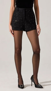 Black high-waisted shorts with scattered rhinestones, paired with sheer black tights and black pointed-toe heels with silver buckles.