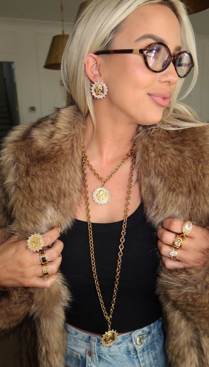 Gold coin pendant necklace with a long chain and matching earrings, rings, and coat collar accents
