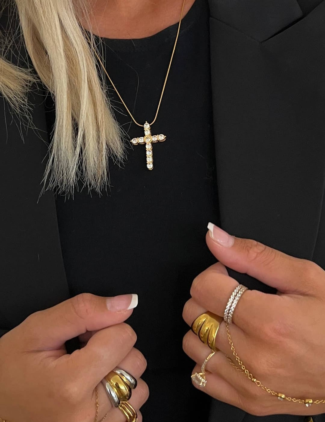 A delicate gold cross necklace adorned with sparkling diamonds, worn against a black blazer.