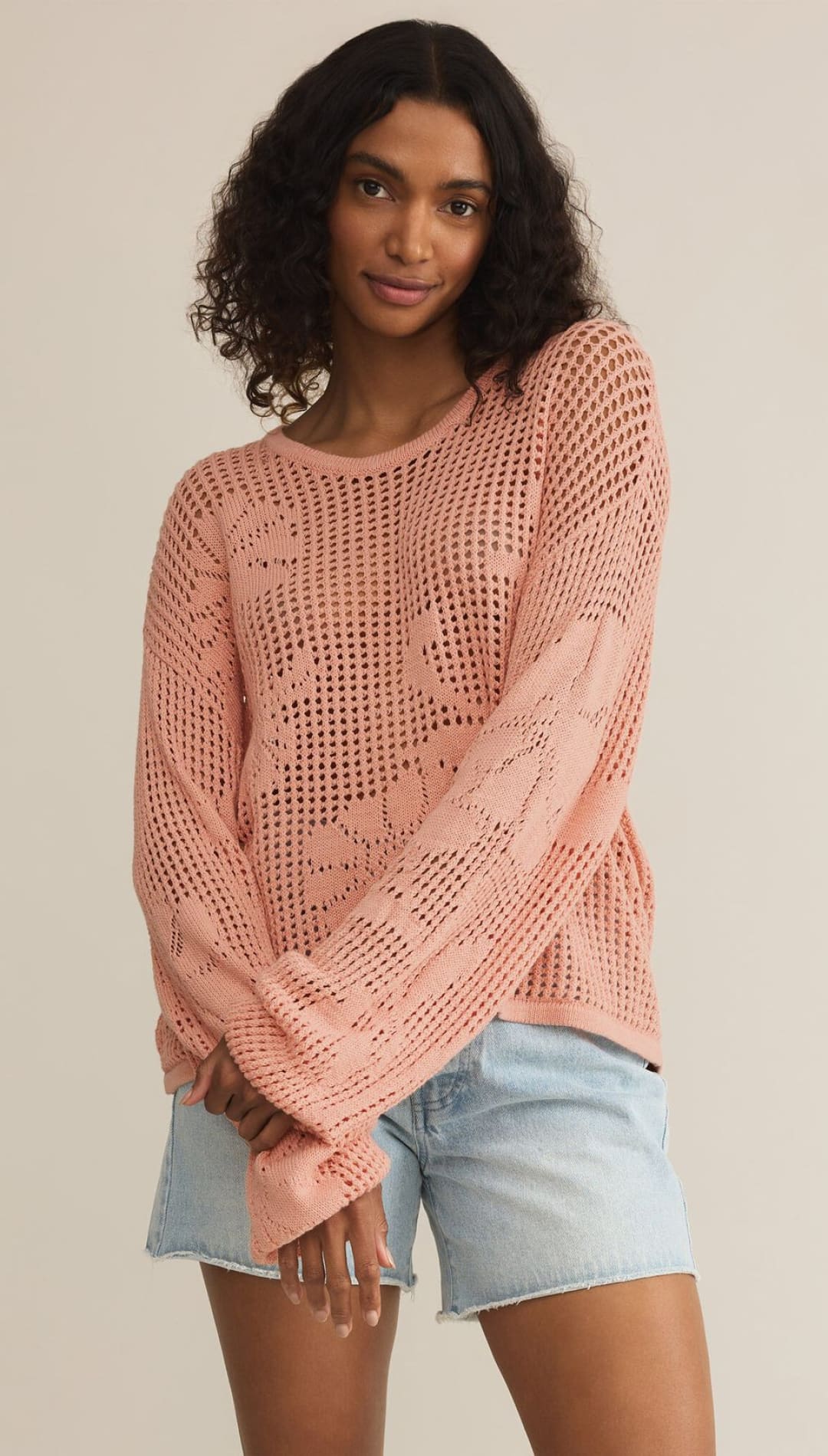 Woman in a pink, open-knit sweater and denim shorts.