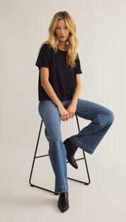 A woman wearing a black short-sleeved t-shirt, wide-leg blue jeans, and black pointed-toe ankle boots.