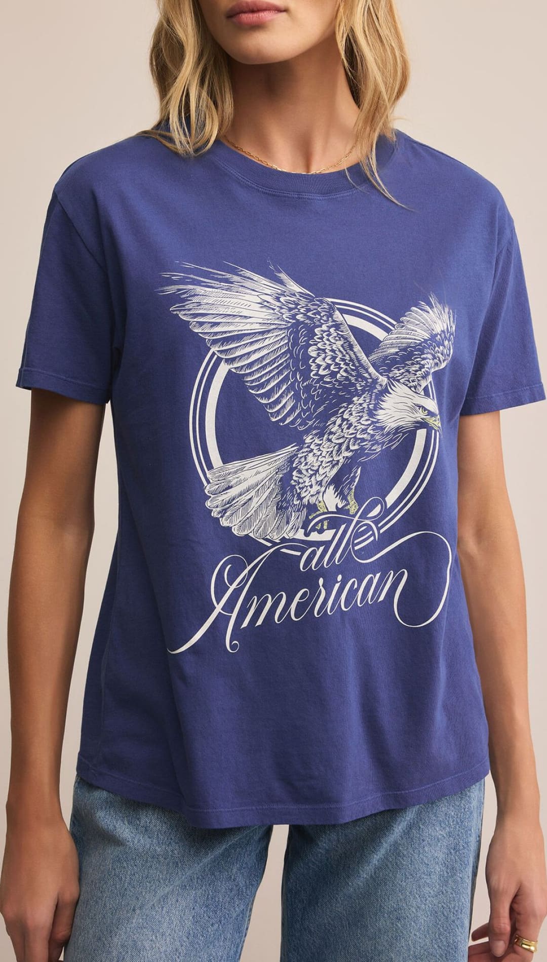 A woman modeling a blue graphic t-shirt featuring a large white eagle design and ’all American’ text.