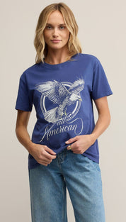 A woman wearing a blue t-shirt with a white graphic of an eagle and the words ’all American’ and light wash blue jeans.