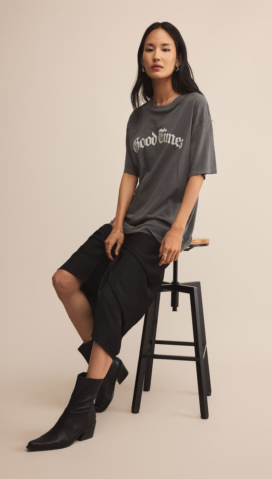 A woman wearing a dark gray oversized graphic t-shirt, black loose-fitting shorts, and black pointed-toe ankle boots.