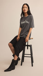 A woman wearing a dark gray oversized graphic t-shirt, black loose-fitting shorts, and black pointed-toe ankle boots.