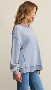 A woman wearing a light blue, long-sleeved crewneck sweatshirt with visible seams and light-wash blue jeans.
